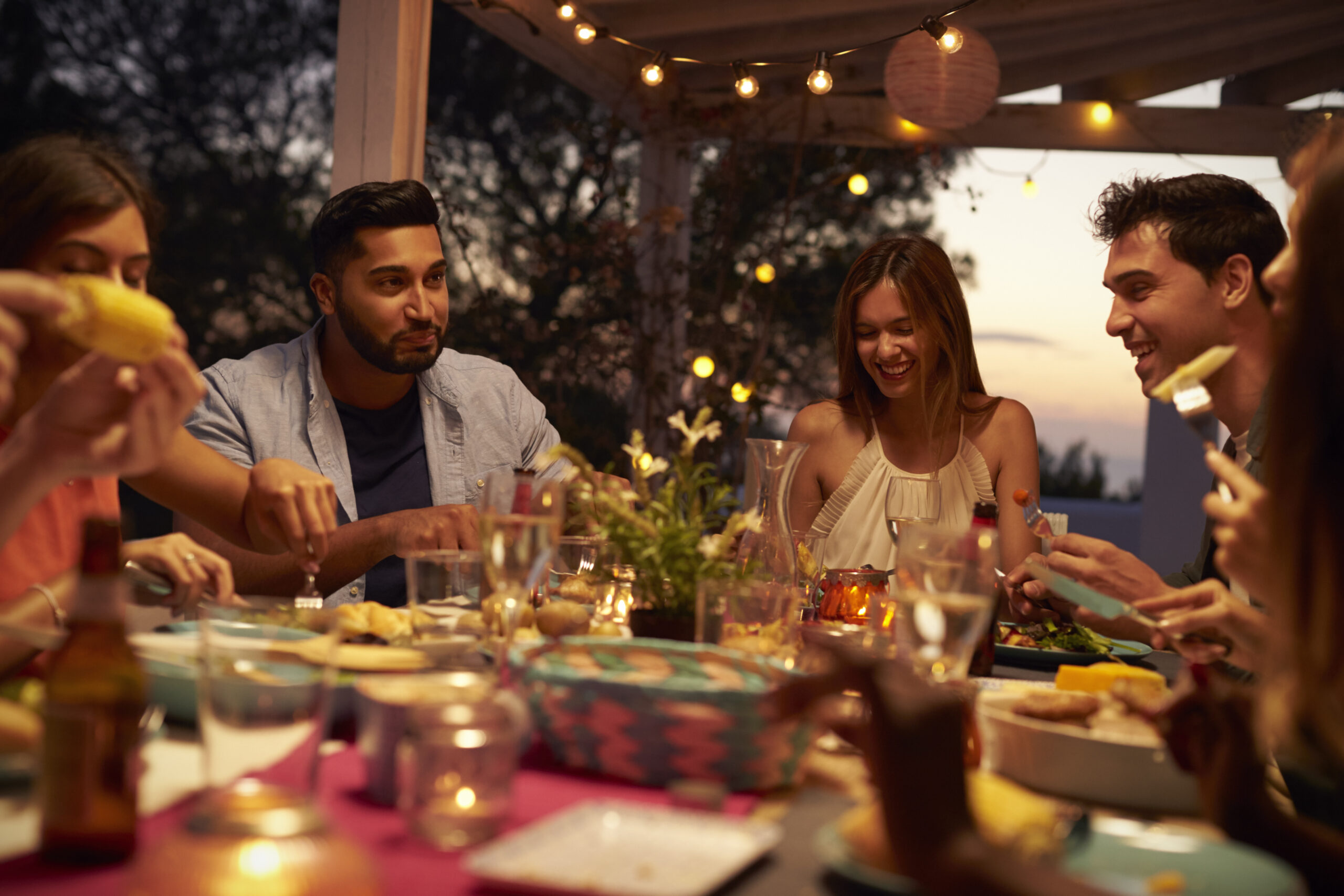 Friends eat and talk at a dinner party on a patio, close up